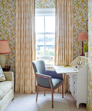 Study with lemon patterned wallpaper, yellow curtains, white desk, armchair, two matching table lamps