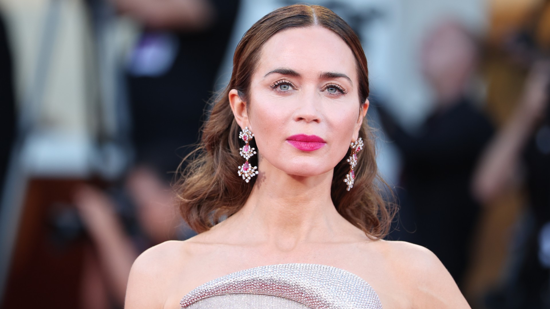 a close up photo of a woman with brown hair wearing red lipstick and posing on a red carpet in front of a crowd of paparazzi