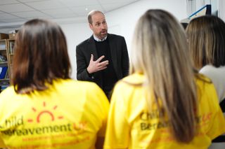 Prince William wearing a blazer talking to a group of young people wearing yellow Child Bereavement UK shirts