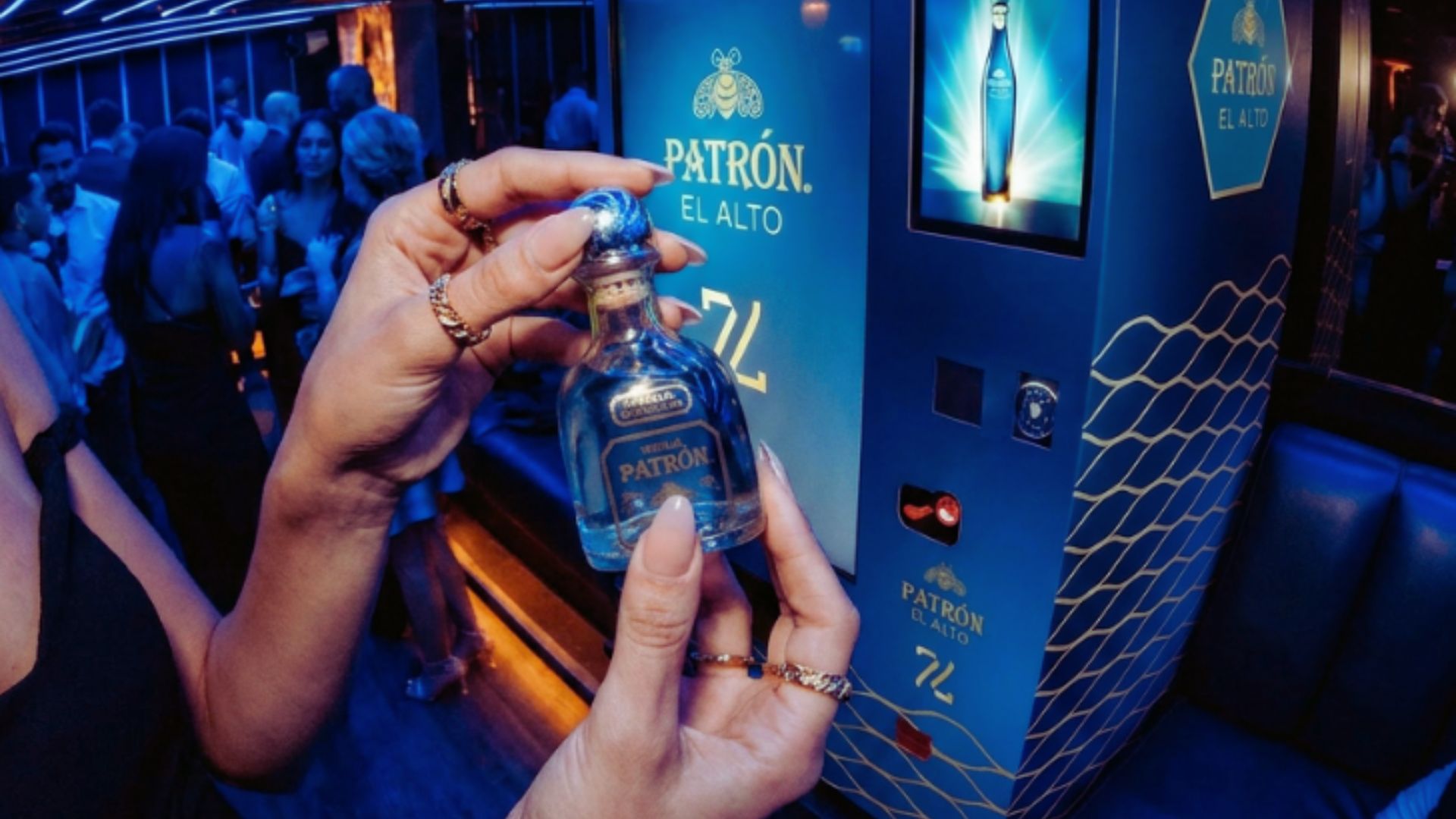 a digital render showing the expected look of the vending machine at 77, with a woman holding one of the miniature 5cl bottles in front of it