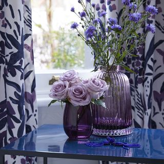 room with floral printed curtains and blue table with flower in vase