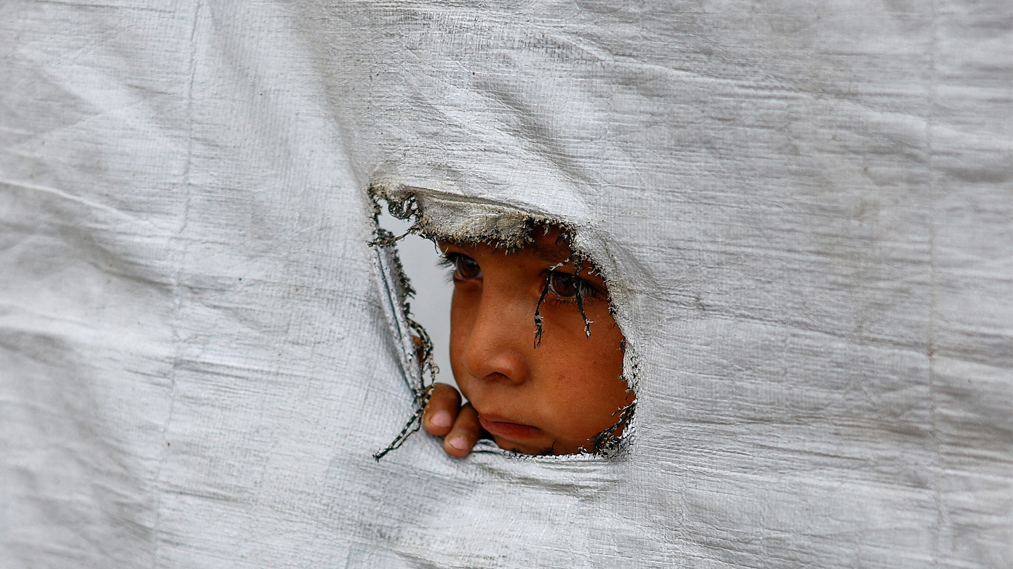 A displaced Palestinian boy peers through the tear in a tent wall, in Gaza City, Palestine