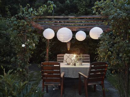 A wooden pergola at dusk with white lampshades hanging from the beams