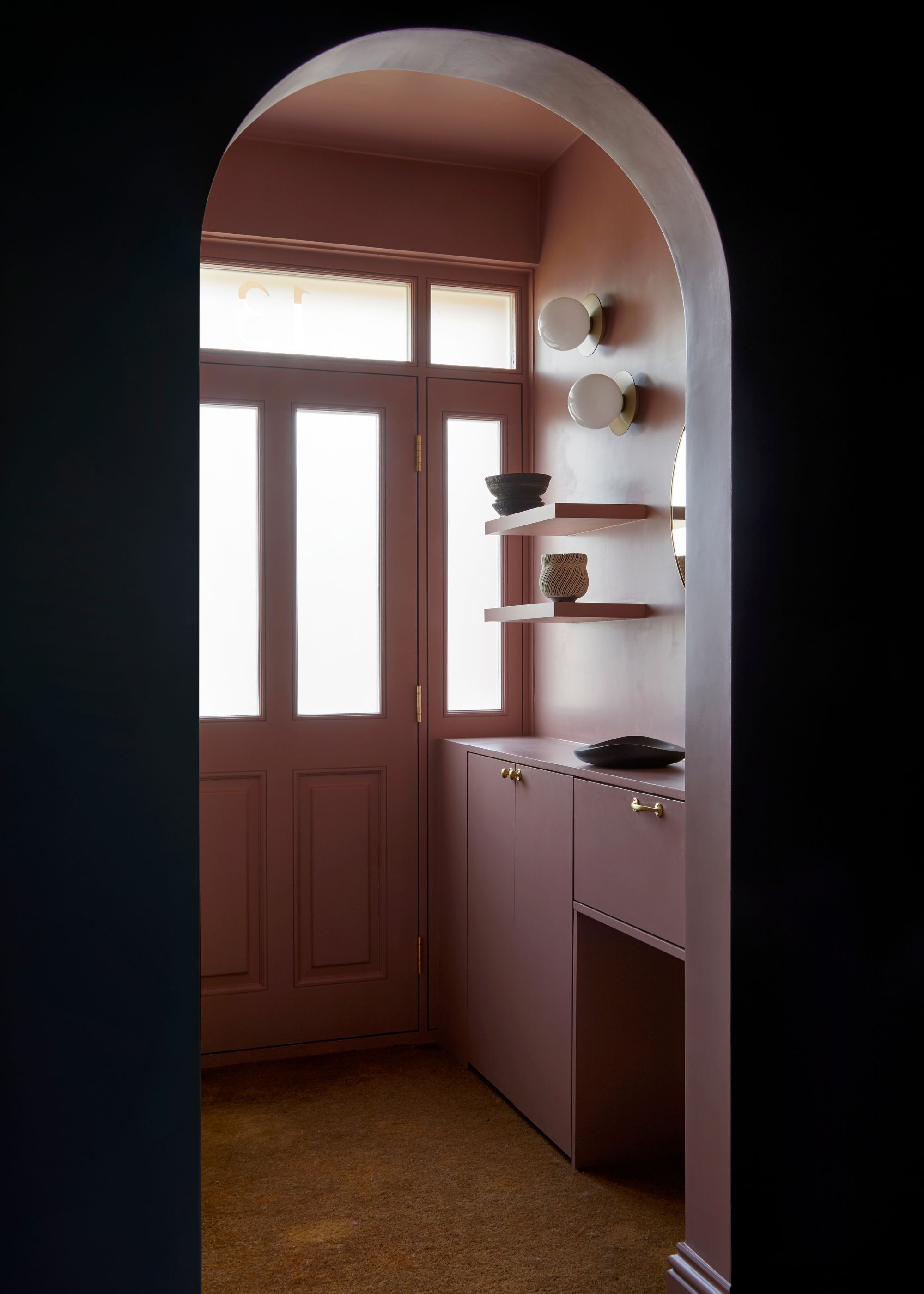 A painted hallway with entryway storage and open shelving as well as an arched doorway leading to the rest of the home