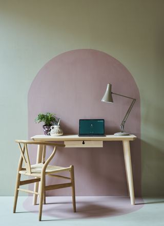 home office with pink and green mural painted wall, blonde wood console table with lamp and desk accessories