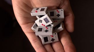 Hand holding a pile of Thumby Game Boy keychain consoles