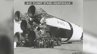 The sheer size of the first stage of the Saturn V can be seen in this photograph from 1960. A group of officials stands in front of the first stage of the Saturn V at the shipping area of the Manufacturing Engineering Laboratory at the Marshall Space Flight Center in Huntsville, Alabama.