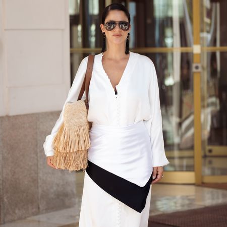 Gili Biegun wears long white and cream silk maxi dress with multiple small buttons, black-and-white silk scarf tied around the waist, oversized raffia beach bag with fringe and brown leather straps, black tassel bead earrings and black Ray-Ban sunglasses during the 79th annual Cannes Film Festival on May 21, 2026 in Cannes, France. (Photo by Raimonda Kulikauskiene/Getty Images)