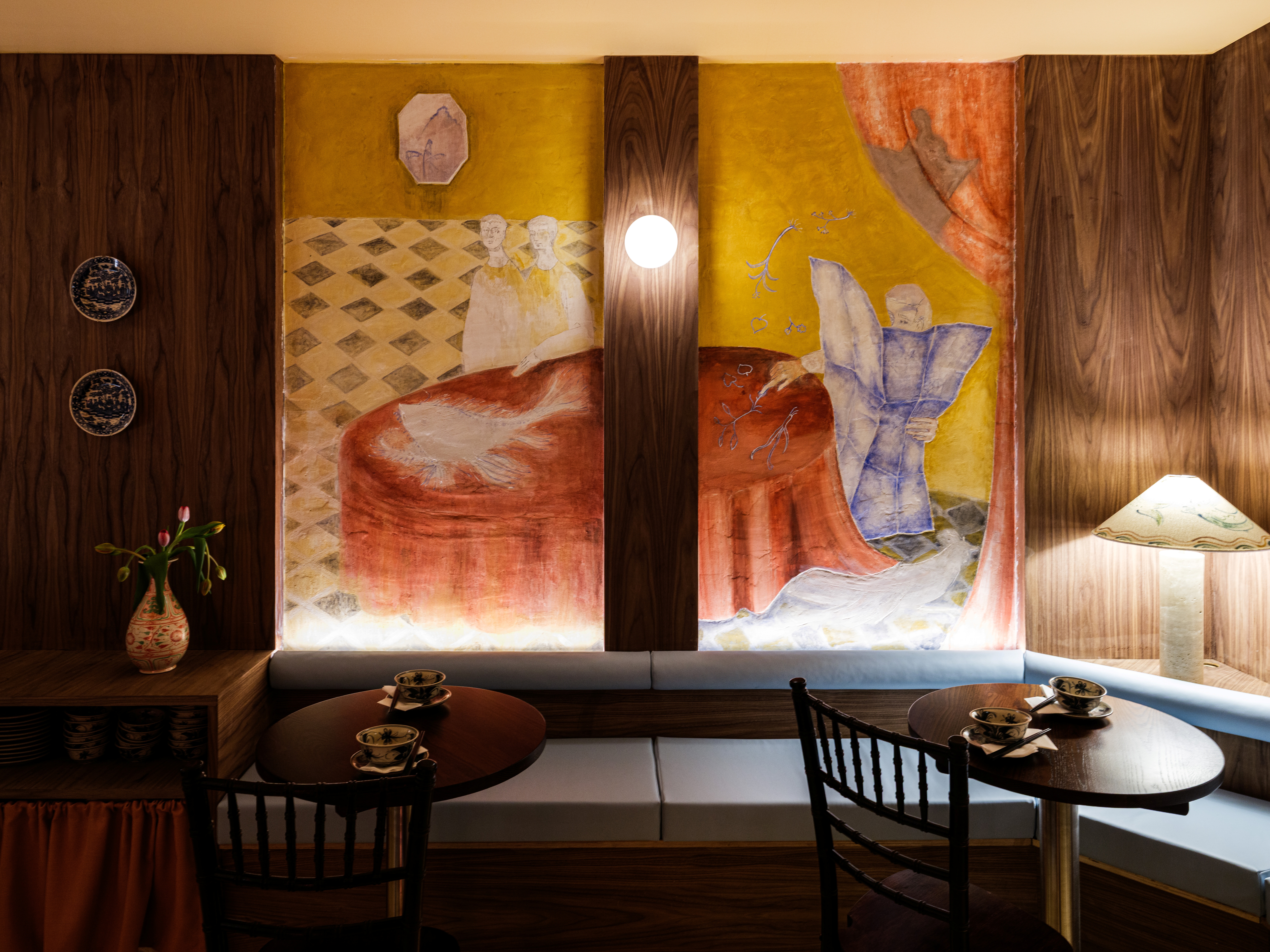 A dramatically lit and designed restaurant pairing cement walls with hand-painted wooden panels, murals, terracotta tiles, chrome accents, and glass blocks.