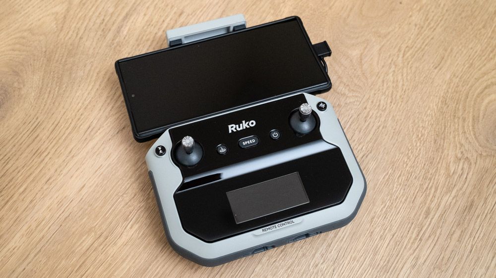 Ruko F11PRO 2 drone controller with a phone attached on a wooden surface