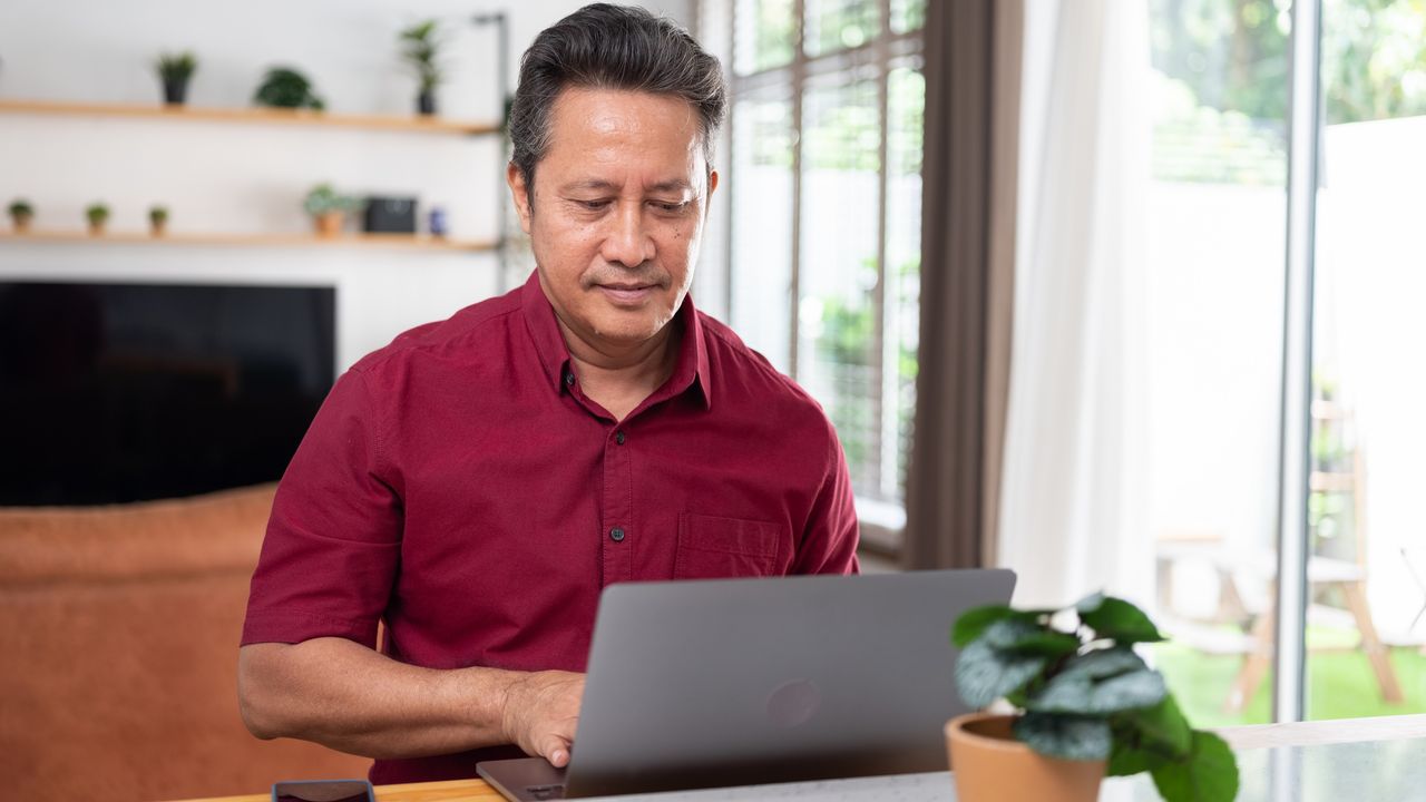 A man uses a laptop at his kitchen table.