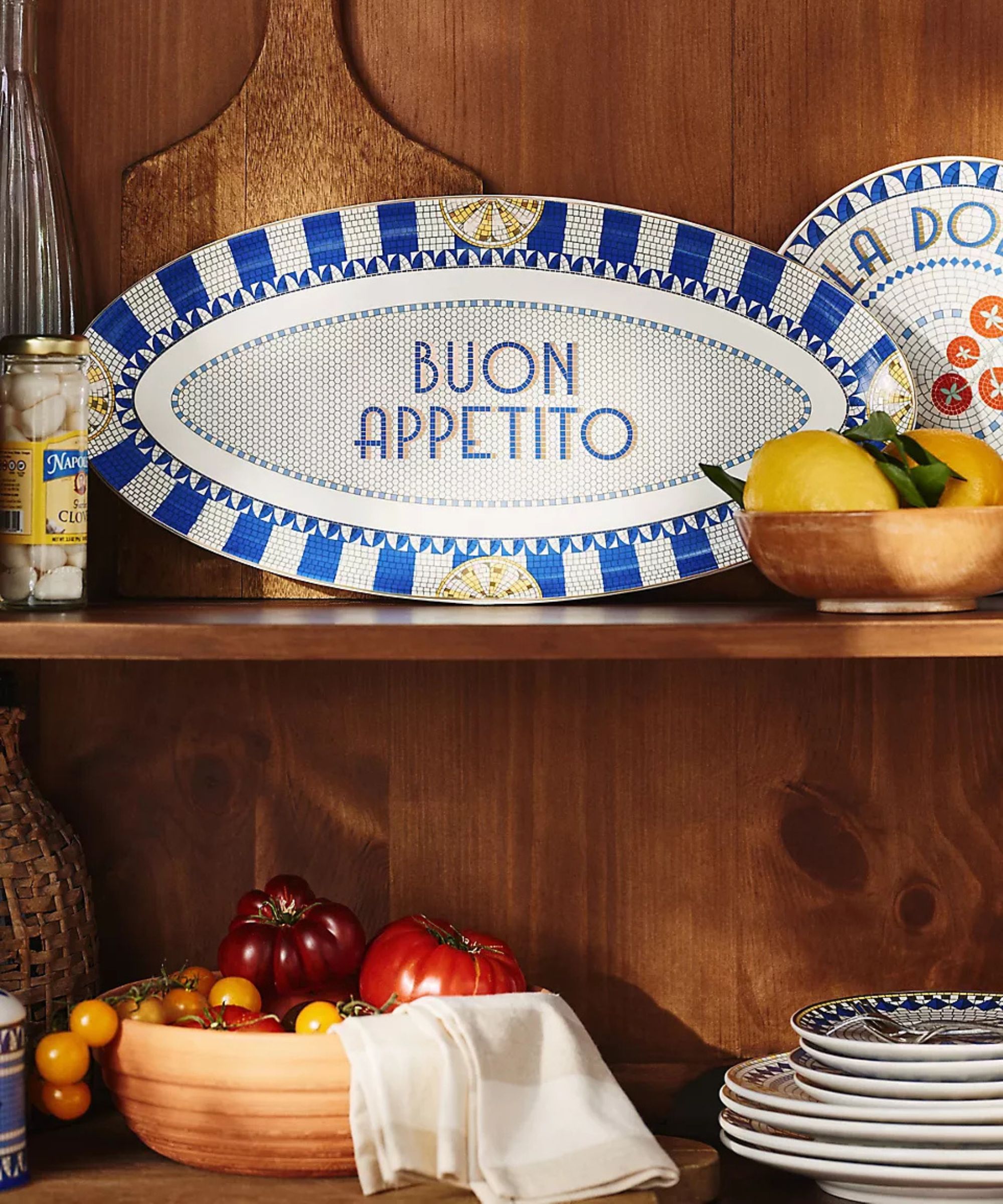 A wooden kitchen shelf filled with Anthropologie's Bistro Tile Collection: Italia Edition plates and platters
