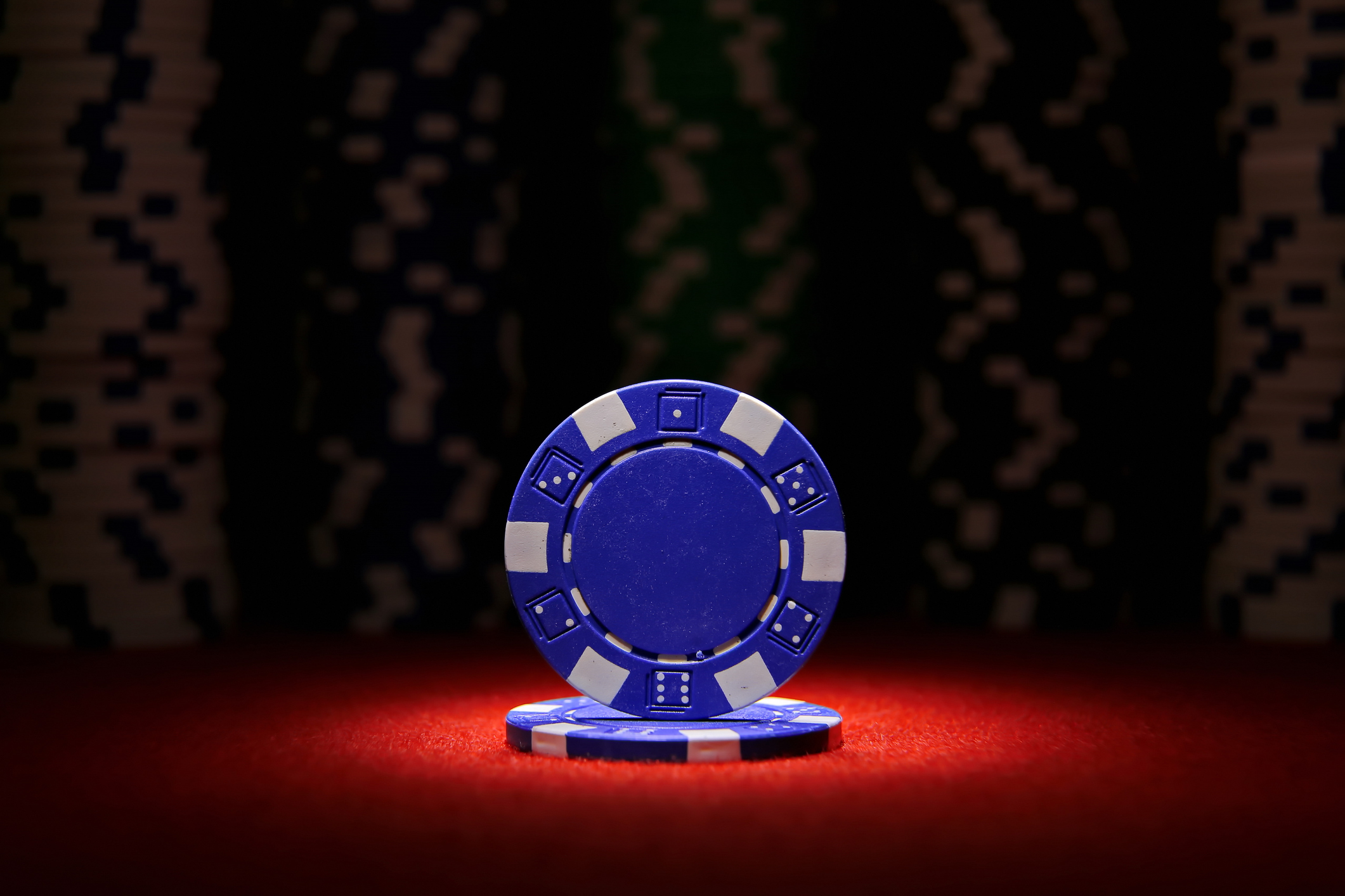 two blue poker chips, stacked under a spotlight