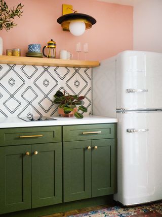 White fridge in a vintage style kitchen with green cabinetry, patterned splashback and salmon walls