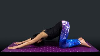 A woman yoga teacher in puppy dog posture isolated on black background