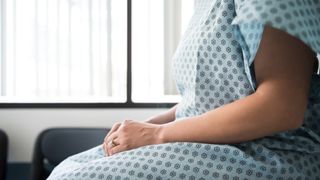 Midsection image of a woman wearing a surgical gown and waiting in a hospital room with her hands on her lap