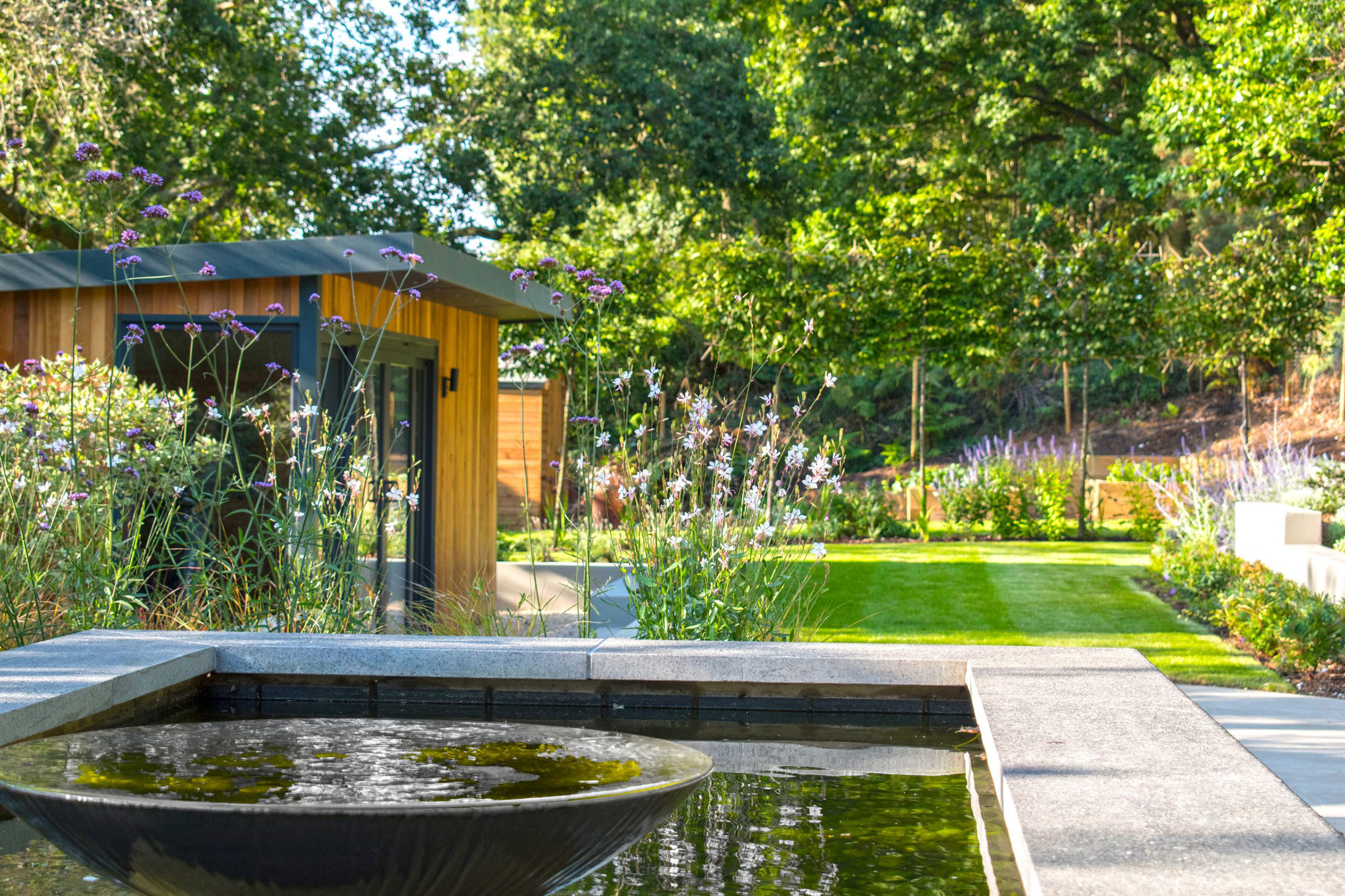 Curated yard space with neat garden, surrounding planting, decking space and slat patio furniture