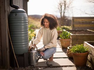 A woman fills a watering can from a rain barrel