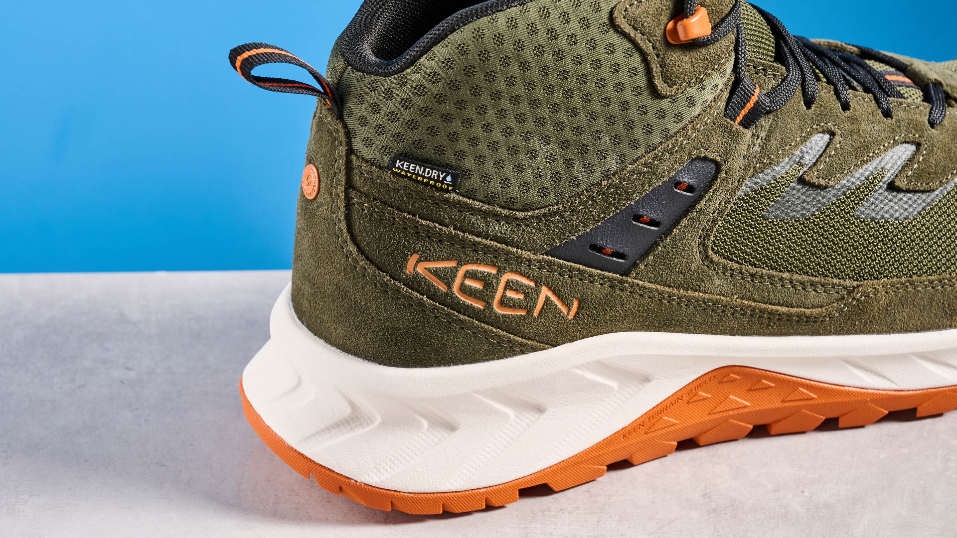 The Keen Hightrail Mid boots in Green on a stone surface against a blue background