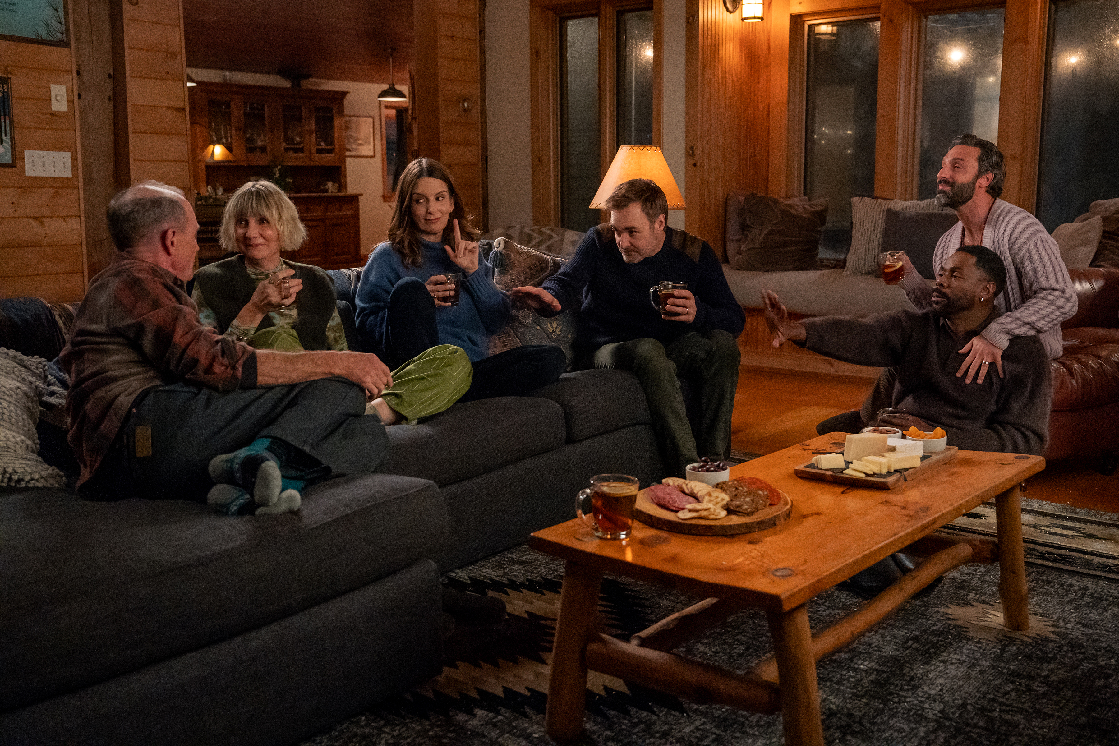 A group of people (l-r: Toby Huss as Terry, Kerri Kenney as Anne, Tina Fey as Kate, Will Forte as Jack, Colman Domingo as Danny, and Marco Calvani as Claude) sit in a living room, in Episode 107 of The Four Seasons.