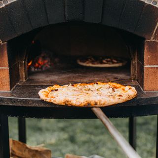 a pizza put in a pizza oven in a garden GettyImages-1686323205