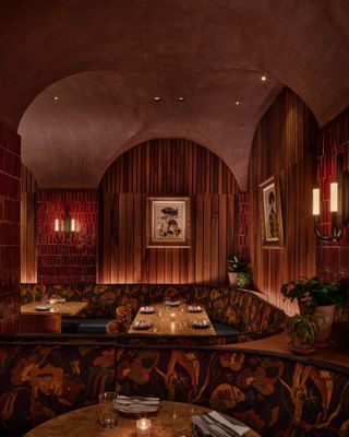 An old jazz bar-inspired hotel restaurant features a warm, upholstery, wood, and plaster decor.