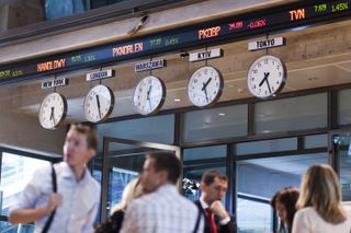 People walking beneath clocks displaying global time zones in the Warsaw Stock Exchange building in Warsaw, Poland.