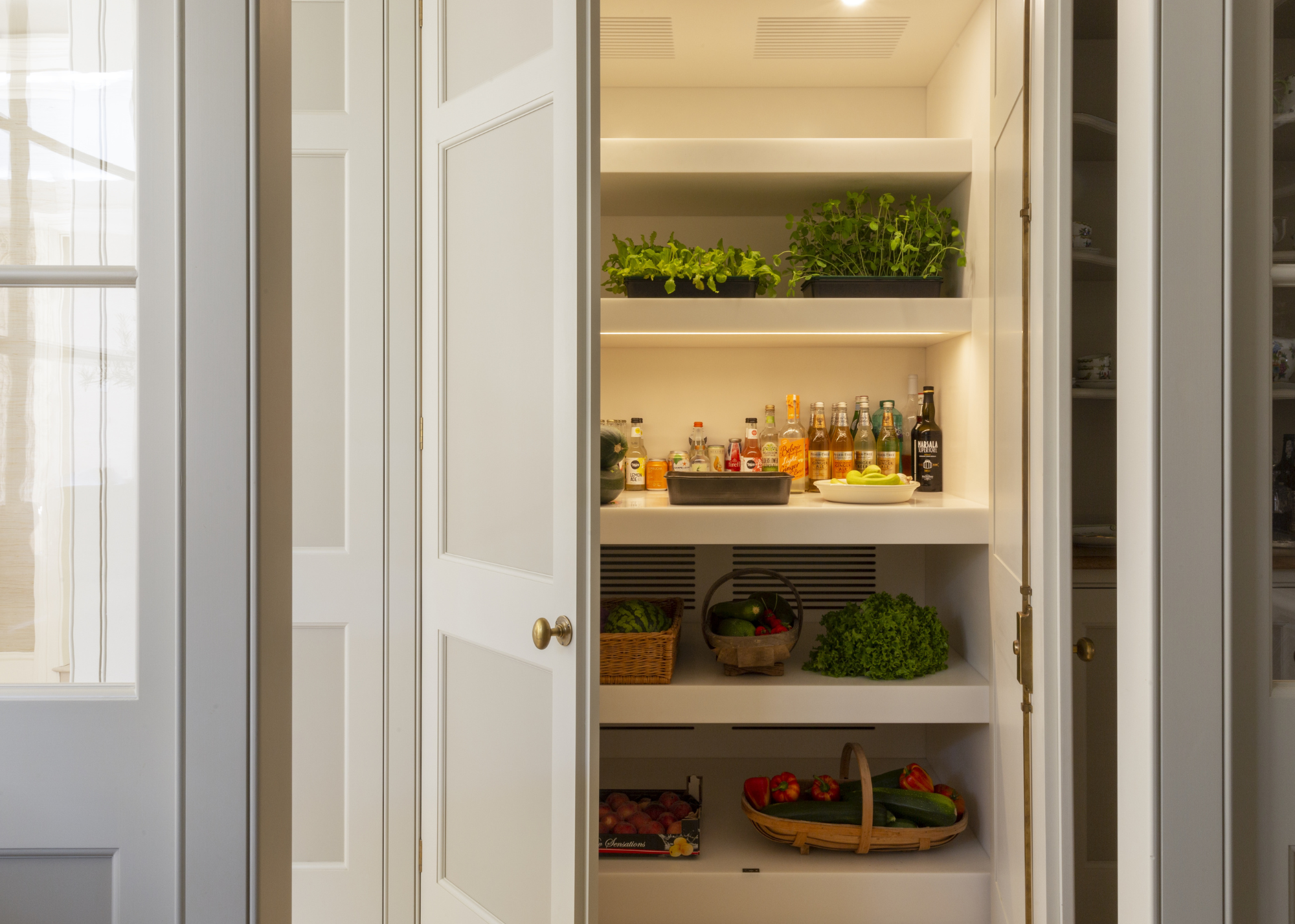 beautiful larder with fresh produce in a corian lined pantry that has lots of fruits, veg and herb across different shelves