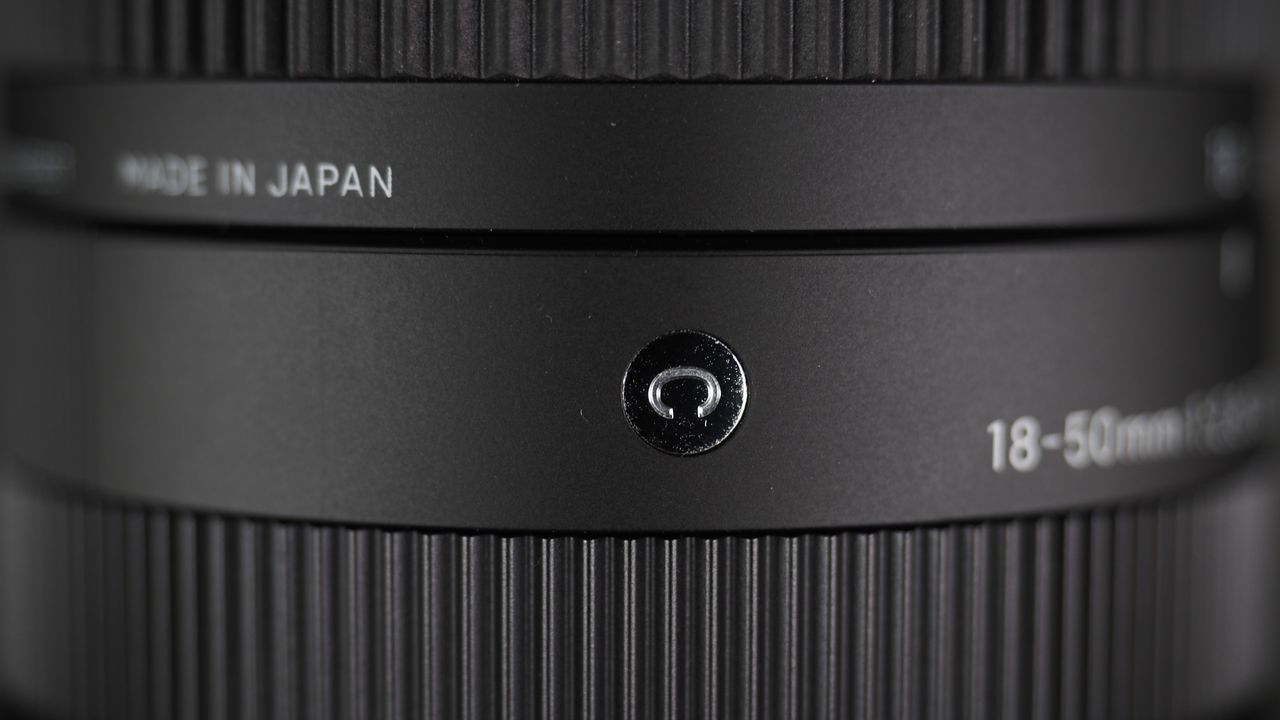 The Sigma 18-50mm f/2.8 DC DN | C Canon RF lens on a wooden surface against a dark background with moody lighting