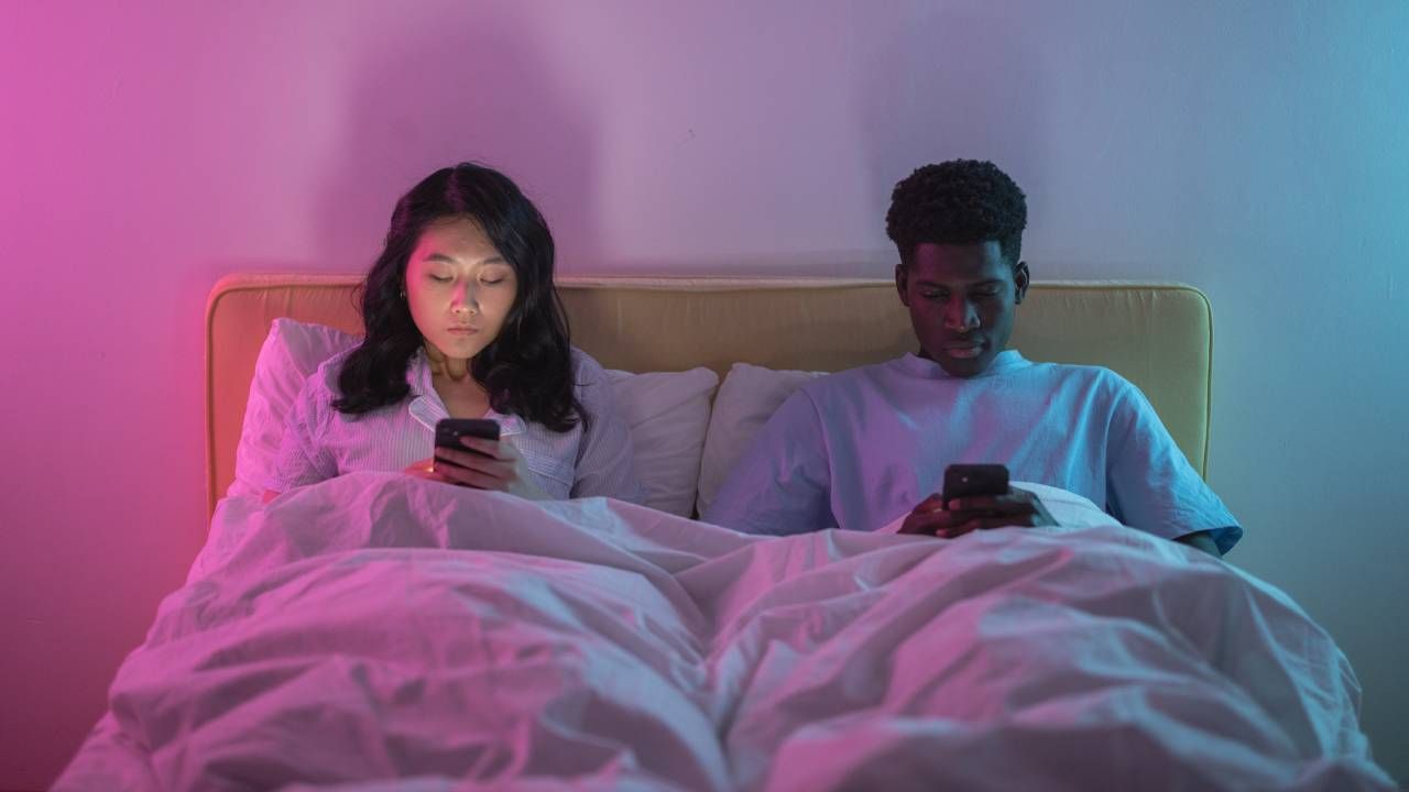 Man and a woman sitting in bed using their phones, sleep &amp; wellness tips