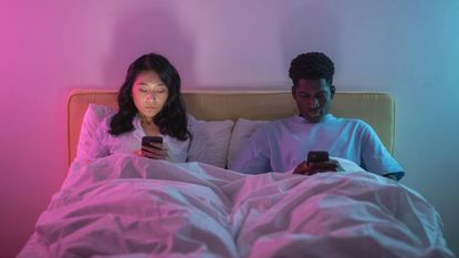 Man and a woman sitting in bed using their phones, sleep & wellness tips