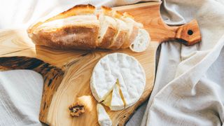 Brie cheese on wooden chopping board next to loaf of white bread