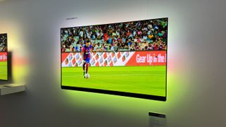 Philips OLED909 TV mounted on a white wall with an image of a footballer on the screen