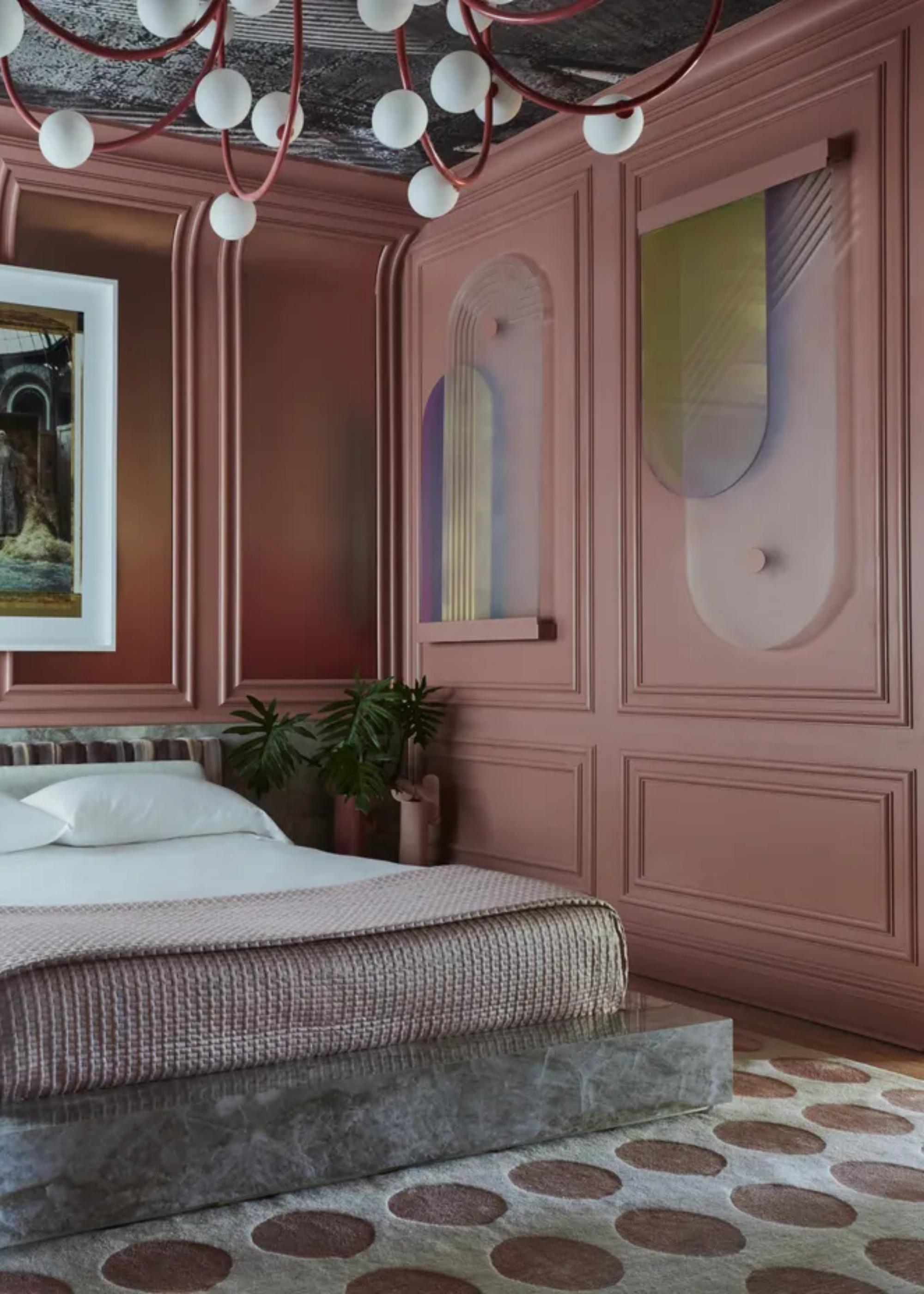 A pink bedroom with colored glass hanging a marble bed base, a potted plant and a white bedscape