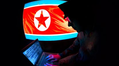 North Korean hacker concept image showing a man in military uniform working on a laptop computer with flag of North Korea pictured on screen in background.