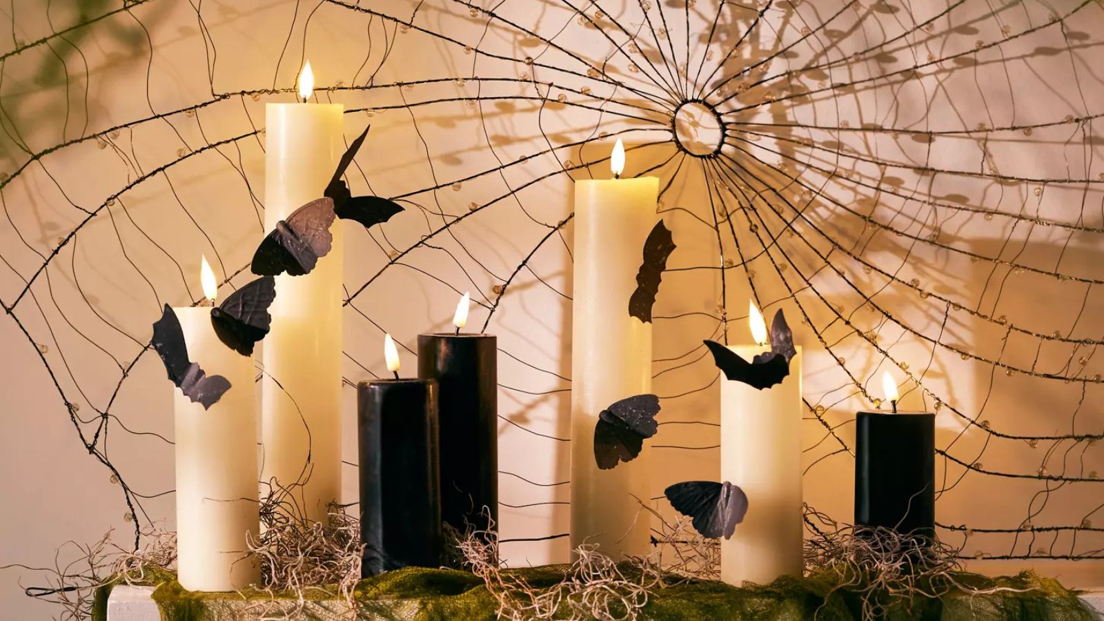 Moss-covered mantlepiece with black and white tapered candles, bat ornaments, and a spider web display
