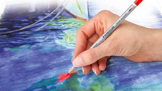 The best coloured pencils are represented by a hand drawing on a wet paper, depicting a pond