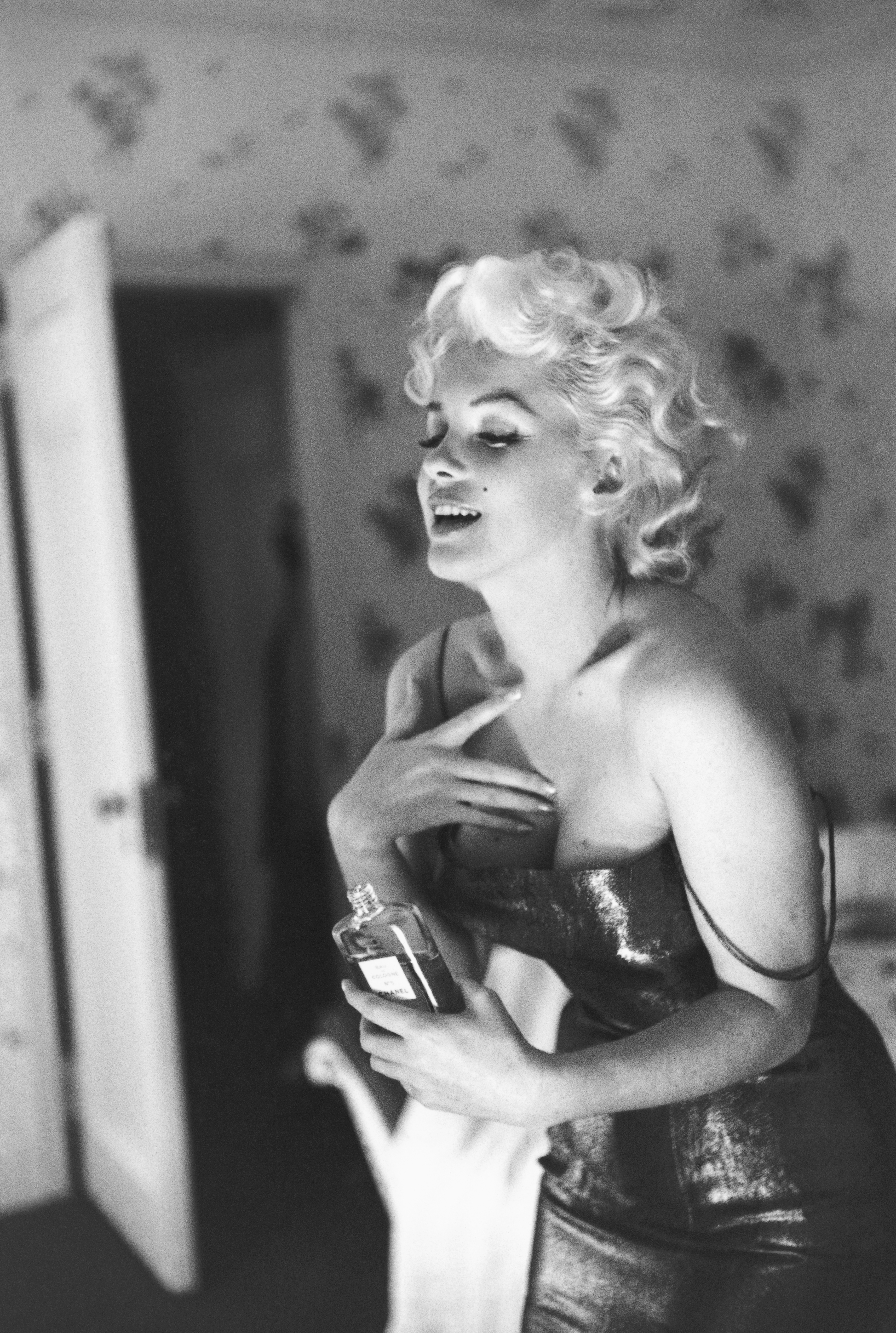 Marilyn Monroe poses with a bottle of Chanel No.5 perfume in a New York hotel room
