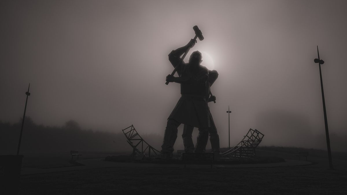 A black-and-white image of The Shipbuilders of Port Glasgow sculpture on a misty day with the sun directly behind the sculptures 