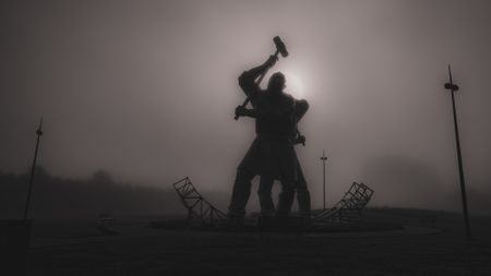 A black-and-white image of The Shipbuilders of Port Glasgow sculpture on a misty day with the sun directly behind the sculptures 