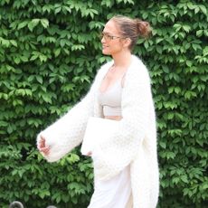 Jennifer Lopez wears a white cardigan with a tan sports bra and white windbreaker pants while walking in the Hamptons