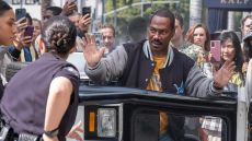 Axel Foley surrenders to two police officers outside an overturned vehicle as a crowd films him on their phones.