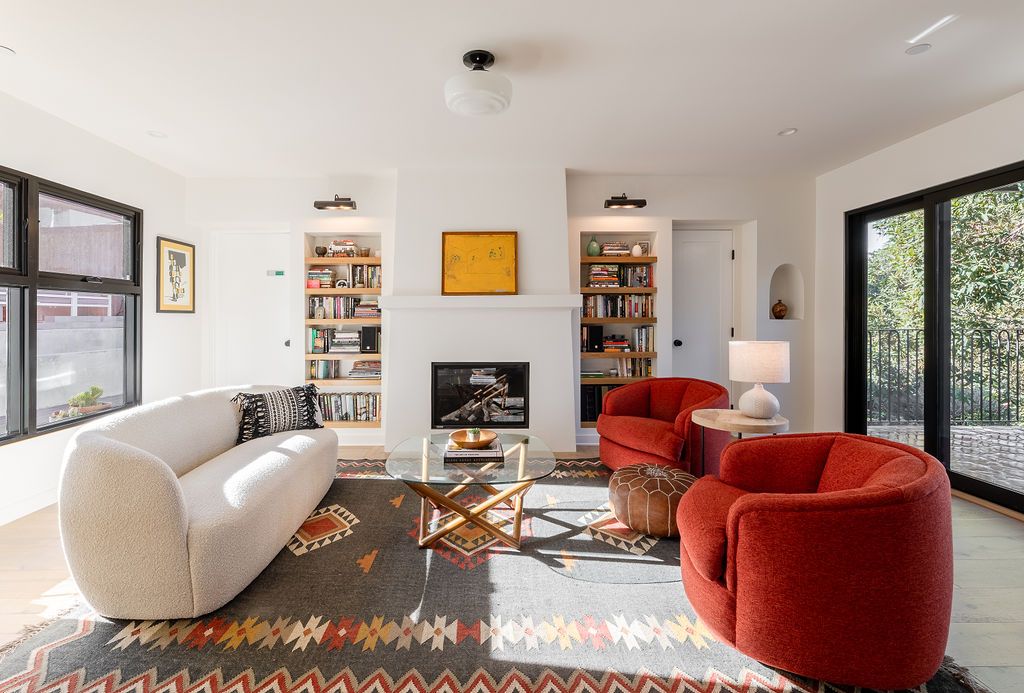 A modern living room with built-in bookcases, a white sofa, and two red armchairs