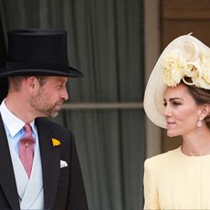 Prince William wearing a top hat talking to Princess Kate wearing a yellow dress and hat