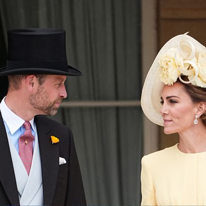 Prince William wearing a top hat talking to Princess Kate wearing a yellow dress and hat