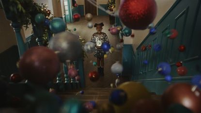 A still shot from the M&amp;S Christmas ad 2024 with baubles falling down the stairs and Skylar standing at the bottom with a snow globe