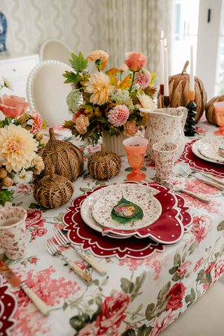 fall table setting with floral tablecloth, red placemats, rattan pumpkins and florals