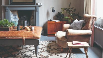 A living room with a a grey-painted fireplace and a vintage leather armchair and ottoman coffee table