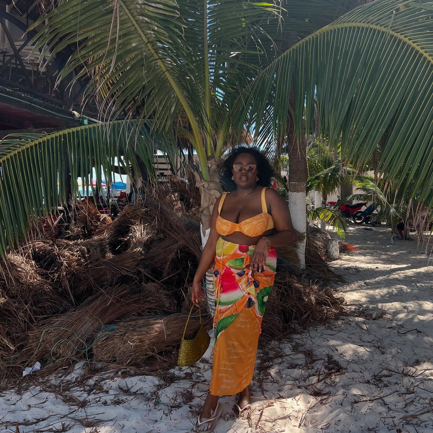 Influencer Iman Leila wears a bright orange sarong wrapped skirt and match orange bikini top carrying a dragon deffusion bag in yellow