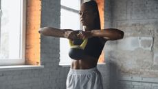 Concentrated young black woman exercising lifting kettlebell to her chest in gym